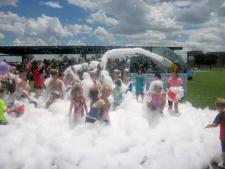 "a group of kids play on a lawn in a huge amount of foam bubbles"