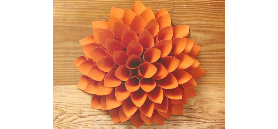 A dahlia flower made of orange paper with each petal a cone shaped piece of paper.